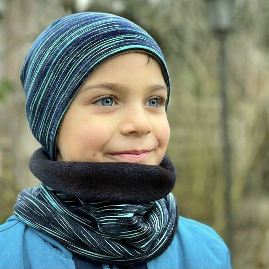 Ein Junge trägt Wollhuhn Öko Shorties, eine zweilagige Wendemütze, ideal für kaltes Wetter. Er lächelt draußen, die Mütze ist handgefertigt und nachhaltig.