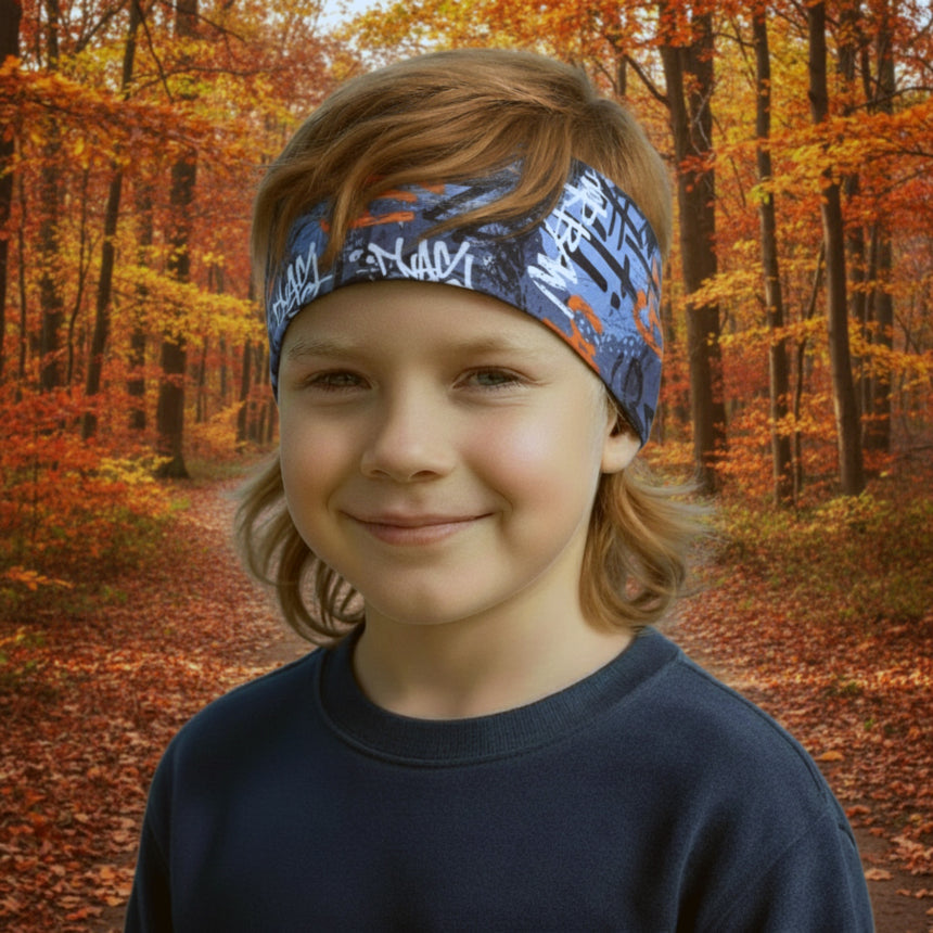 Kind im Wald trägt Wollhuhn Elastisches Öko Stirnband, Jersey zweilagig breit, Aquarellsprenkel Weiß/Blau, handgemacht in Deutschland, ideal für Herbstaktivitäten.