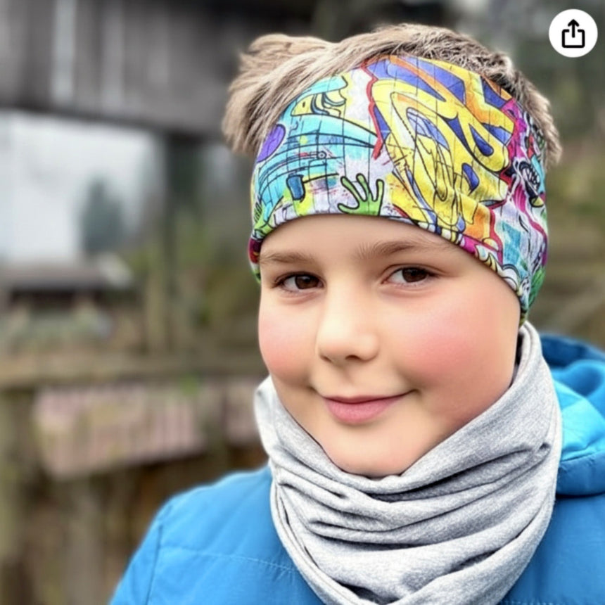 Kind mit Wollhuhn Elastisches Öko Stirnband, zweilagig und breit, in Graffiti-Design, trägt blauen Wintermantel und grauen Halswärmer. Perfekt für Outdoor-Aktivitäten.