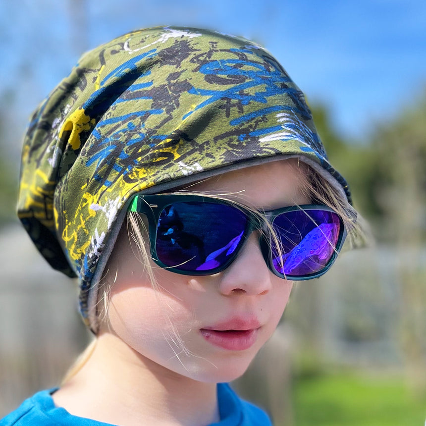 Kind mit Sonnenbrille und Bandana trägt die Wollhuhn Öko Long Beanie, Wendemütze, ideal für ganzjähriges Tragen, aus weichem, formbeständigem Baumwolljersey, handgefertigt.