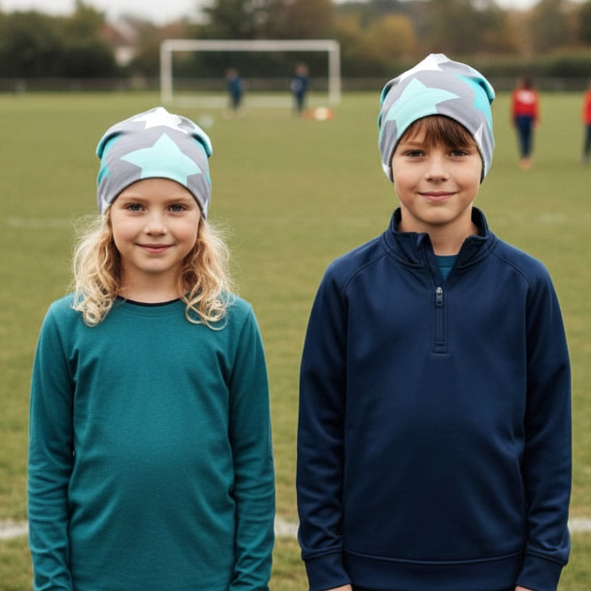 Zwei Kinder tragen Wollhuhn Öko Long Beanie / Wendemütze mit großen Sternenmotiv auf einem Sportfeld, ideal für ganzjähriges Tragen dank wärmendem, zweilagigem Design.