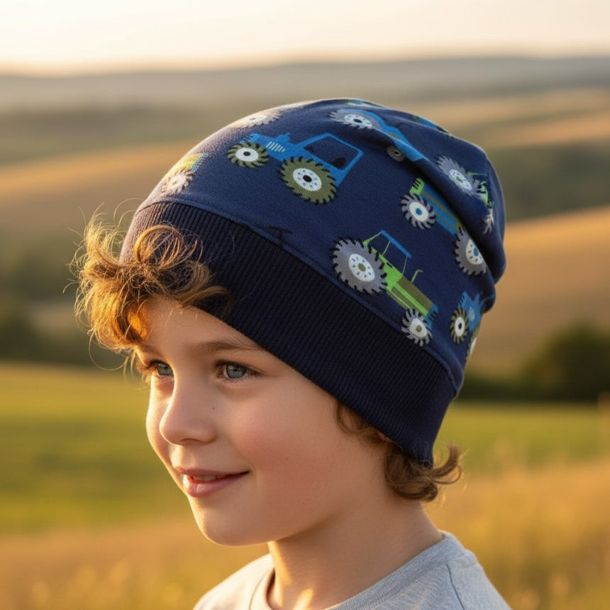 Kind trägt Wollhuhn Dünne Öko Beanie-Mütze Sommer/Übergang Einlagig Traktor/Trecker Dunkelblau, lächelt in sonniger Landschaft. Beanie ist handgemacht, bequem und dehnbar.
