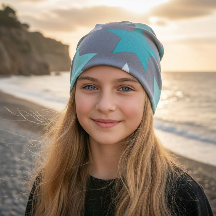 Mädchen am Strand mit Wollhuhn Öko Shorties Wendemütze, zweilagig und mit Sternenmuster, ideal für aktive Kinder, handgefertigt in Süddeutschland.
