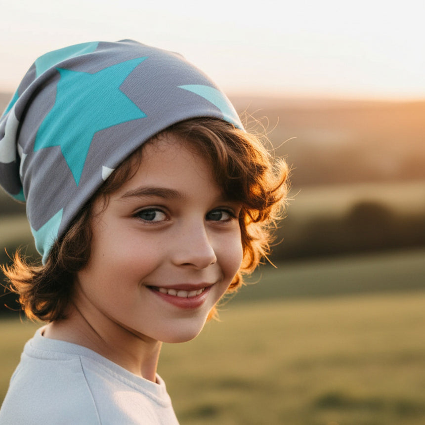 Kind im Freien trägt Wollhuhn Öko Long Beanie / Wendemütze mit großen Sternen, lächelt zur Kamera. Handgefertigt, bequem, ideal für alle Jahreszeiten.
