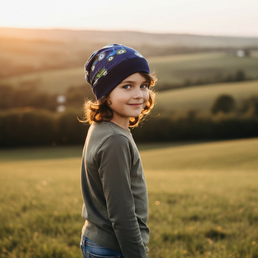 Kind in Wollhuhn Dünne Öko Beanie-Mütze Sommer/Übergang, lächelt im Sonnenuntergang. Handgemachte, atmungsaktive Beanie, ideal für aktive Kinder, gefertigt in Deutschland.