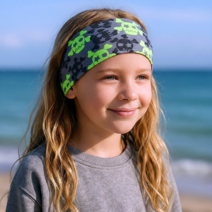 Mädchen am Strand trägt Wollhuhn Elastisches Öko Stirnband mit Totenkopf-Muster, ideal für Outdoor-Aktivitäten, handgemacht aus nachhaltiger Bio-Baumwolle.
