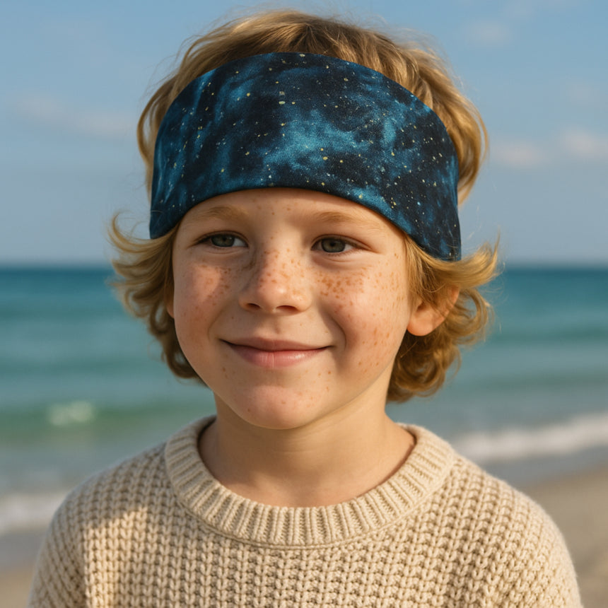 Junge mit Wollhuhn Stirnband am Strand; handgemachtes, elastisches Öko-Stirnband aus Jersey, ideal für Outdoor-Aktivitäten, gefertigt in Deutschland.