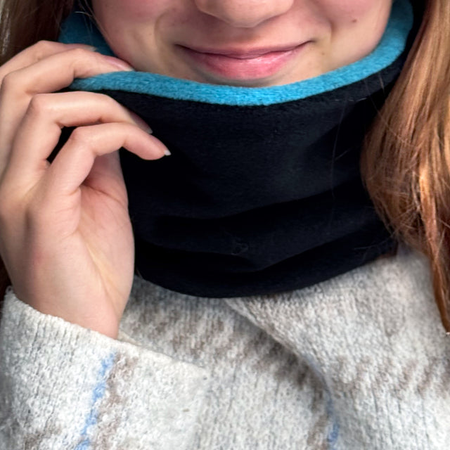 Frau trägt Wollhuhn WINTER Halstuch/Schlupfschal „Unser Wärmster“, doppellagiger Fleece in Schwarz/Türkis, ideal für kalte Tage. Handgemacht in Deutschland.