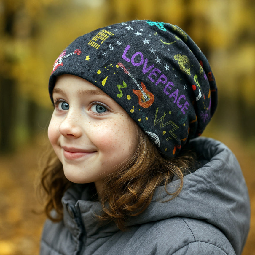Ein lächelndes Kind trägt die Wollhuhn Öko Long Beanie mit bunten Doodles, geeignet für Herbsttage. Handgemacht, wendbar, komfortabel und ideal für Kinder.