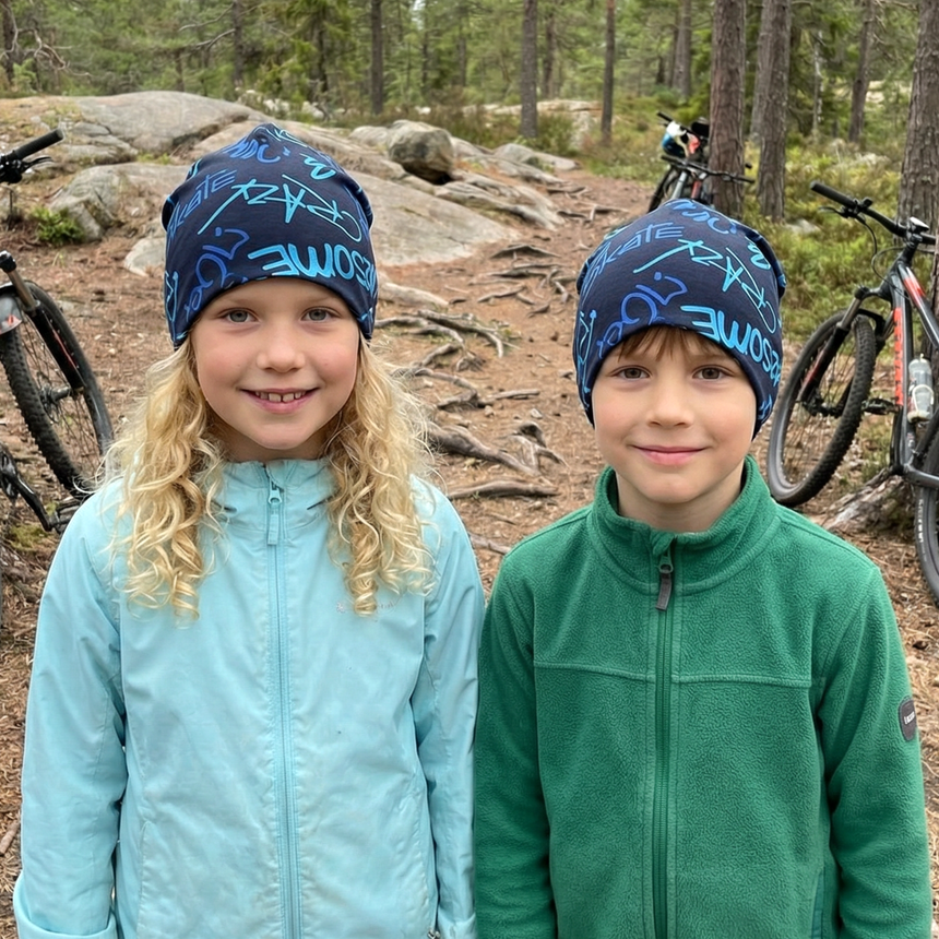 Zwei Kinder tragen die Wollhuhn Öko Long Beanie, Wendemütze, Ganzjährig, Zweilagig, Cool Music Blautöne, auf einem Waldweg, lächelnd vor ihren Fahrrädern.