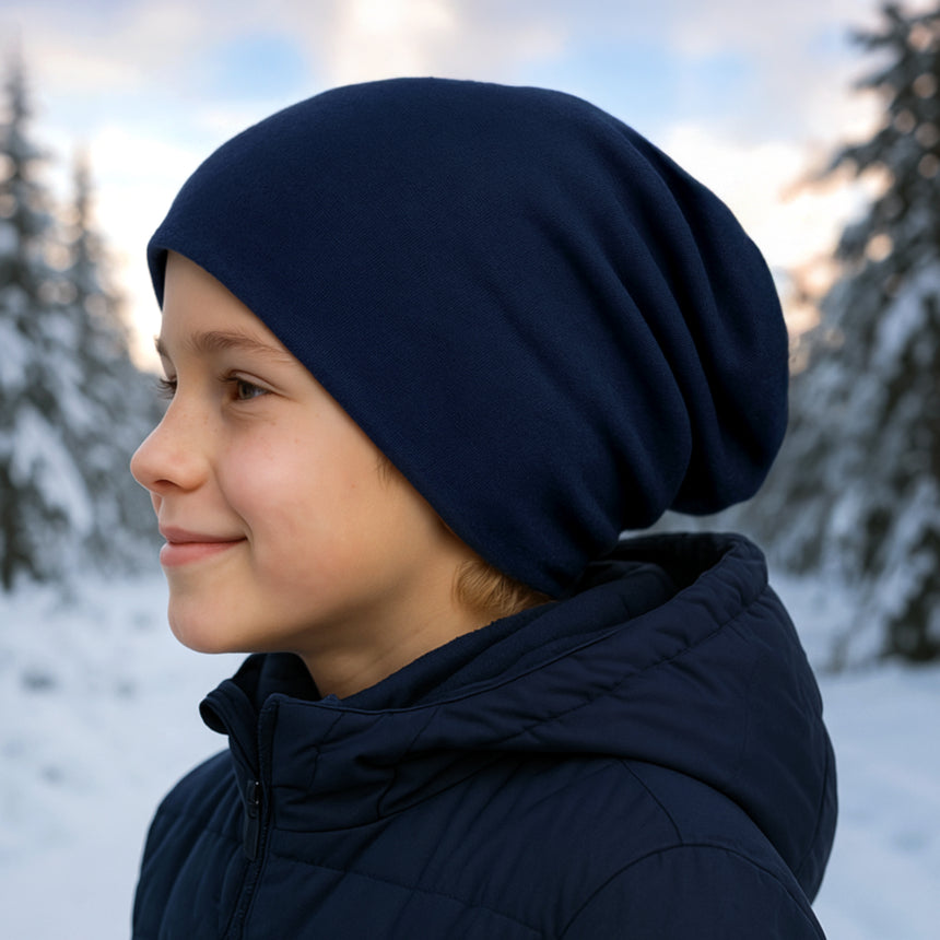 Kind mit Wollhuhn Öko Long Beanie, zweilagig und wendbar, im Schnee. Mütze ist aus weichem Baumwolljersey, ideal für Winter und Übergang.