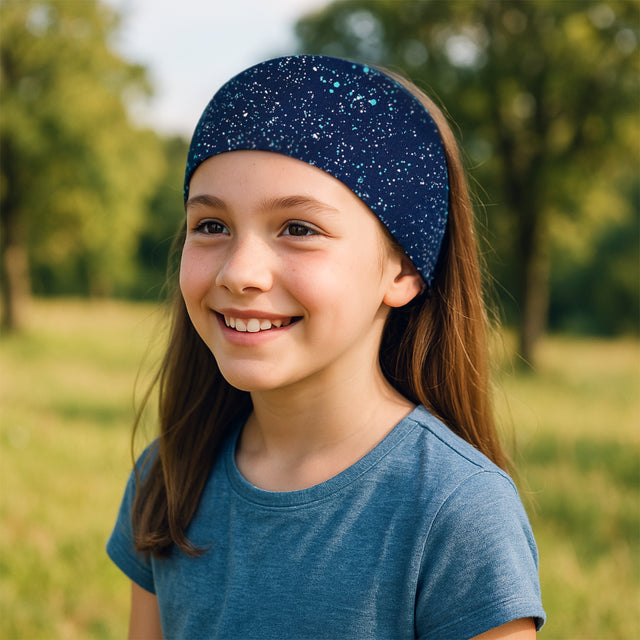 Mädchen trägt Wollhuhn Elastisches Öko Stirnband, Jersey zweilagig, breit, ideal für Outdoor-Aktivitäten, handgefertigt aus Bio-Baumwolle, weich und vielseitig.