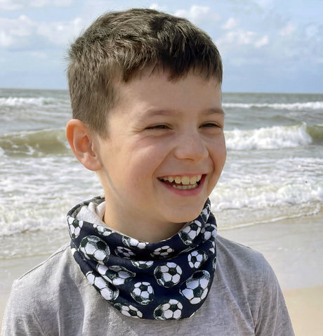 Junge am Strand trägt Wollhuhn leichtes Jersey Halstuch mit Fußballmuster, perfekt für Übergangszeiten, handgemacht in Deutschland, schützt vor Wind und Sonne.