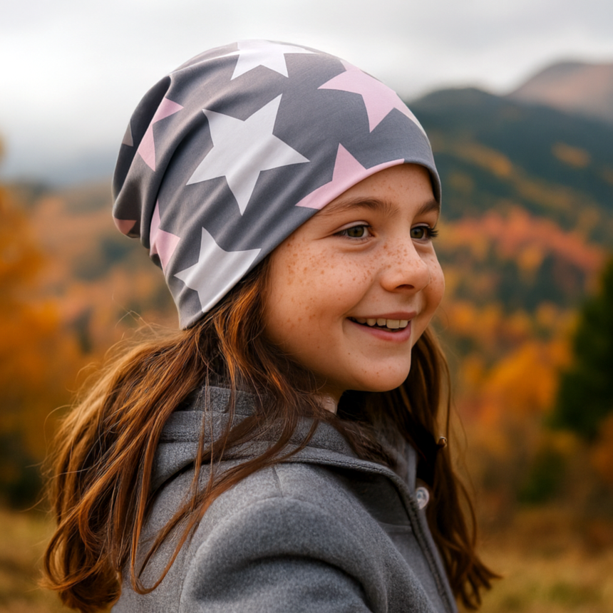 Mädchen mit Wollhuhn Öko Long Beanie, Wendemütze, Grau mit großen weißen und rosa Sternen, im herbstlichen Freien, zeigt stilvollen und bequemen Sitz.