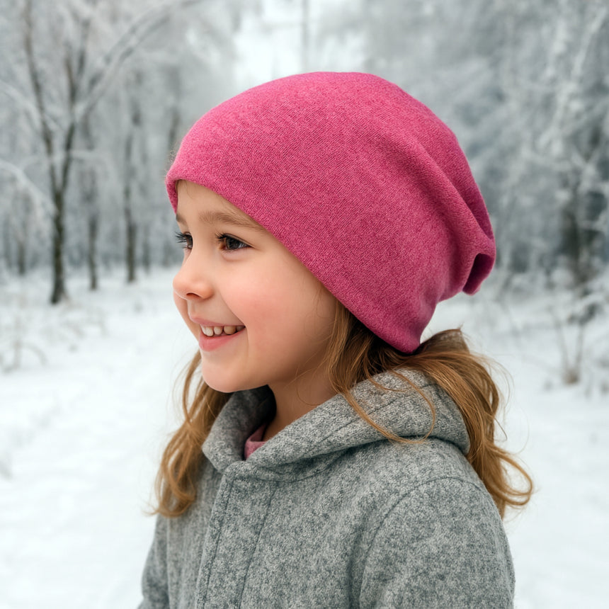 Kind im Schnee mit Wollhuhn Öko Long Beanie, zweilagig und wendbar, in Beere. Ideal für kalte Tage, hält warm und ist bequem zu tragen.