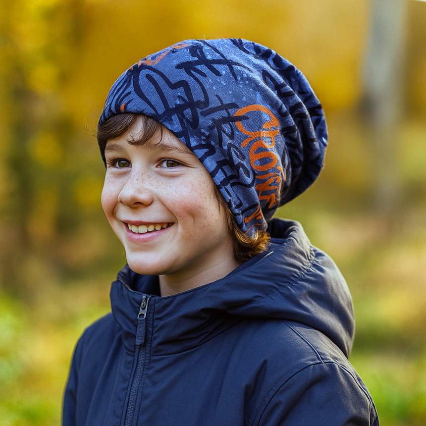Ein Junge trägt eine Wollhuhn Öko Long Beanie / Wendemütze, Ganzjährig, Zweilagig, Skater Grau/Orange im Herbstpark. Ideal für Komfort und Wärme.