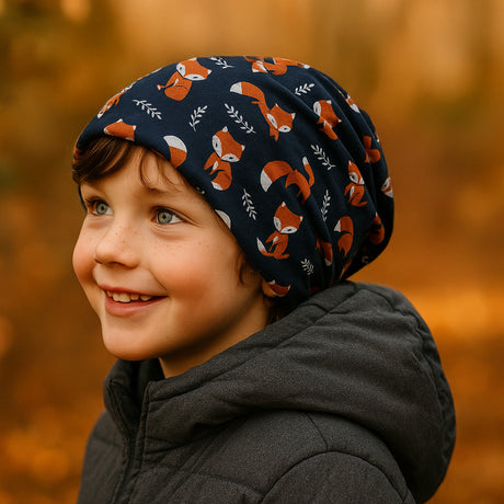 Ein lächelnder Junge trägt die Wollhuhn Öko Long Beanie, dunkelblau mit Fuchs-Muster, ideal für Herbsttage, aus weichem, wendbarem Öko-Jersey, zweilagig.