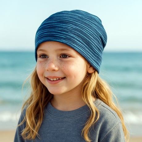 Mädchen mit blauem Beanie von Wollhuhn, lächelnd. Handgefertigte Wendemütze aus Öko-Jersey, ideal für aktive Kinder. Perfekt für Freizeit und Sport.