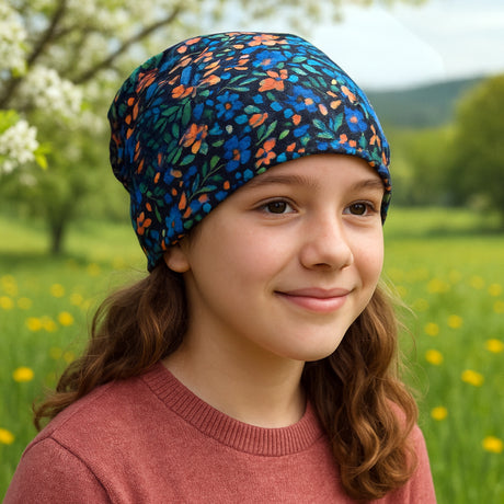 Mädchen trägt Wollhuhn Öko Shorties Beanie im Blumenfeld, zeigt lässigen, komfortablen Stil für aktive Kinder; ideal für Freizeit und Sport.