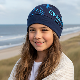 Mädchen am Strand trägt Wollhuhn Dünne Öko Beanie-Mütze Sommer/Übergang Einlagig Cool Music Blau, handgemacht aus dehnbarem, sanftem Öko-Jersey, ideal für Kinder.