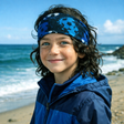 Junger Junge am Strand trägt Wollhuhn Elastisches Öko Stirnband, zweilagig, mit Fußballmuster in Blautönen. Perfekt für Freizeit und sportliche Aktivitäten.