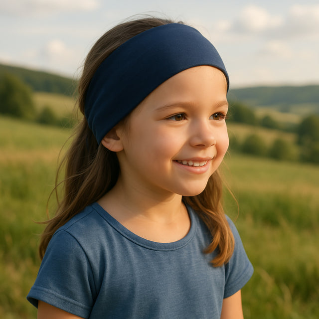 Mädchen trägt ein Wollhuhn Elastisches Öko Stirnband, zweilagig und breit, in Dunkelblau, lächelnd auf einer Wiese. Ideal für Outdoor-Aktivitäten.