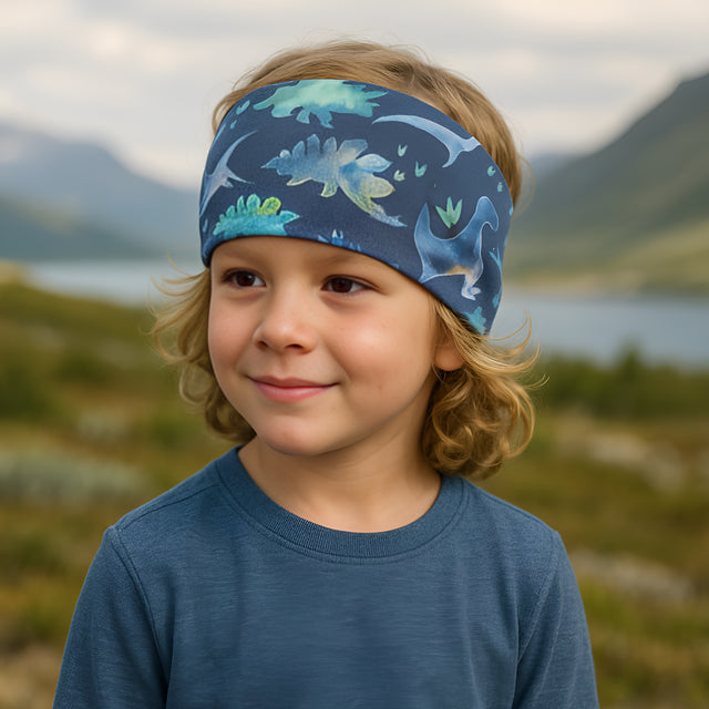 Kind trägt ein Wollhuhn Elastisches Öko Stirnband, zweilagig und breit, aus Jersey, in Blautönen mit Dinosaurier-Design. Ideal für Outdoor-Aktivitäten und handgefertigt.