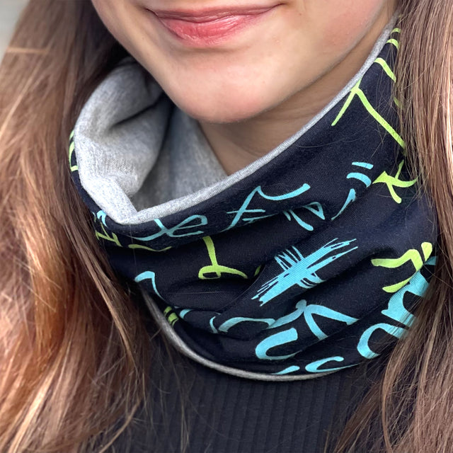 Frau trägt Wollhuhn LONG Loop, Jersey- oder Fleecefutter, Cool Music Schwarz; handgemachter, bequemer Schal, ideal für Schutz vor Wetter, passt Kindern und Erwachsenen.