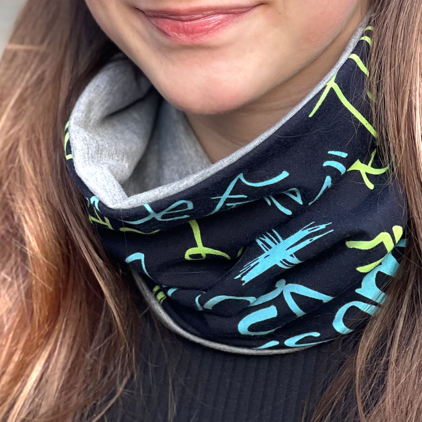 Frau trägt Wollhuhn LONG Loop, Jersey- oder Fleecefutter, Cool Music Schwarz; handgemachter, bequemer Schal, ideal für Schutz vor Wetter, passt Kindern und Erwachsenen.