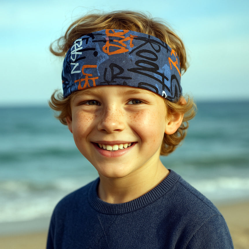 Ein Junge am Strand trägt das Wollhuhn Elastisches Öko Stirnband, das handgemacht, zweilagig und vielseitig für Outdoor-Aktivitäten geeignet ist.