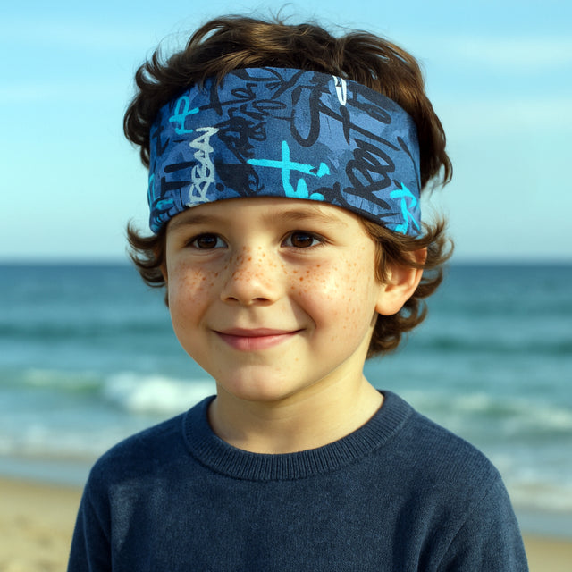 Junge am Strand trägt das Wollhuhn Elastisches Öko Stirnband aus Jersey, handgemacht, weich und vielseitig, ideal für Outdoor-Aktivitäten.
