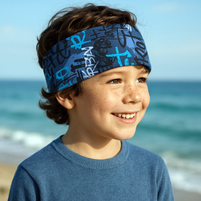 Junge am Strand trägt ein Wollhuhn Elastisches Öko Stirnband, zweilagig und breit, ideal für Outdoor-Aktivitäten, handgemacht aus Bio-Baumwolle.