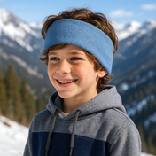 Junge trägt Wollhuhn Elastisches Öko Stirnband Fleece Zweilagig Breit Einfarbig Jeansblau Melange, steht lächelnd in verschneiter Berglandschaft.