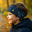 Seitliches Profil eines Kindes im Freien, trägt ein Wollhuhn Elastisches Öko Stirnband Jersey Zweilagig Breit Splatter Dunkelblau, ideal für Herbstspaziergänge.