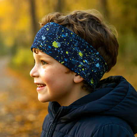 Seitliches Profil eines Kindes im Freien, trägt ein Wollhuhn Elastisches Öko Stirnband Jersey Zweilagig Breit Splatter Dunkelblau, ideal für Herbstspaziergänge.
