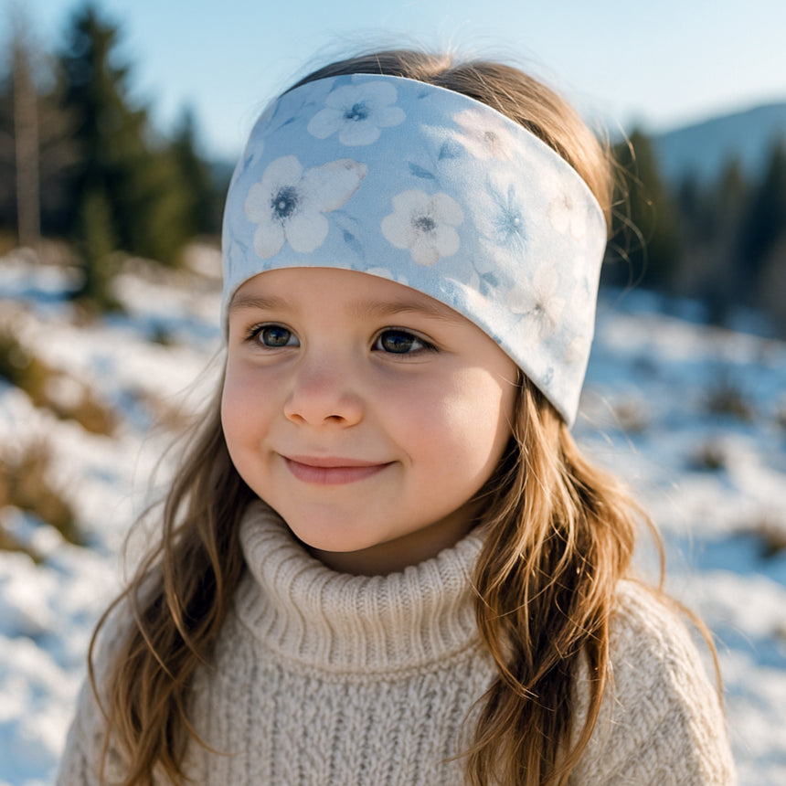 Mädchen trägt ein Wollhuhn Elastisches Öko Stirnband/Haarband Jersey Zweilagig Breit in der Schneelandschaft, lächelnd und mit einem handgemachten, bequemen Stirnband aus Bio-Baumwolle.