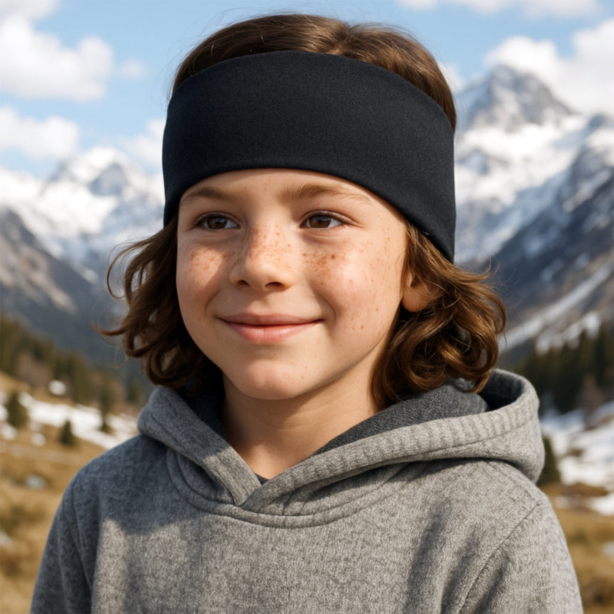 Junger Junge mit Wollhuhn Stirnband in dunklem Blau im schneebedeckten Gebirge, trägt grauen Hoodie. Perfekt für kalte Tage, handgemacht in Deutschland.
