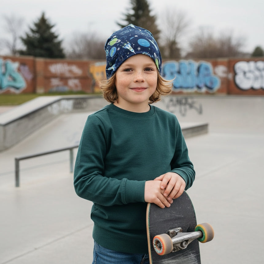 Kind trägt Wollhuhn Öko Long Beanie / Wendemütze, Ganzjährig, Zweilagig, Space/Rakete Dunkelblau im Skatepark, passend zu Sweatshirt und Jeans, ideal für Freizeitaktivitäten.