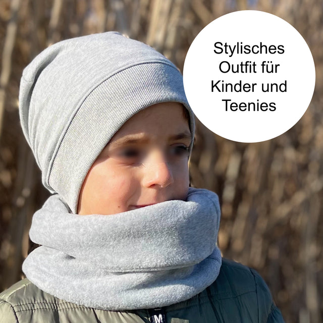 Kind trägt Wollhuhn Dünne Öko Beanie-Mütze, handgefertigt aus weichem Öko-Jersey. Ideal für Übergangszeiten, bequem, mitwachsend, schützt Ohren. Perfekt für Freizeitaktivitäten.