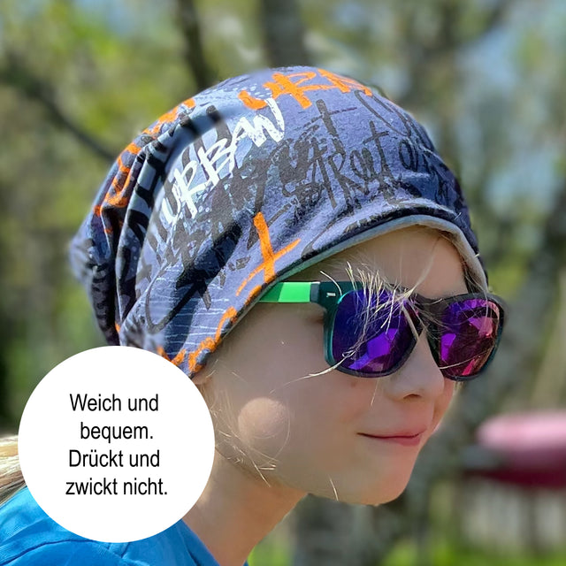 Mädchen mit Sonnenbrille und Bandana trägt die Wollhuhn Öko Long Beanie, eine zweilagige, wendbare Mütze, ideal für ganzjähriges Tragen.