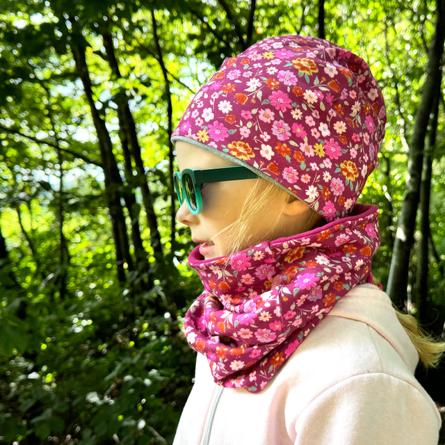 Eine Frau im Wald trägt den Wollhuhn LONG Loop, Blumen Beere, als Schal. Der handgemachte Loop bietet Komfort und Schutz vor Wettereinflüssen.