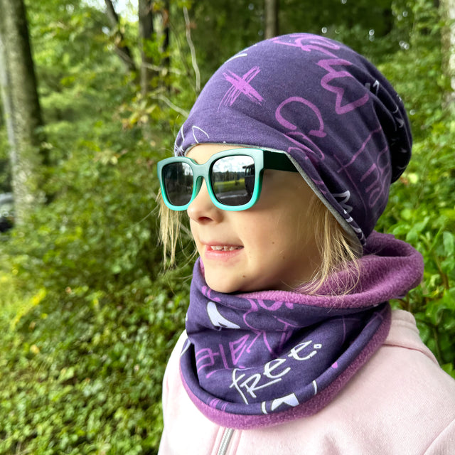 Mädchen trägt Wollhuhn Öko Long Beanie Wendemütze, zweilagig, bequem und modisch. Perfekt für ganzjähriges Tragen, ideal für Kinder, violette Beanie.