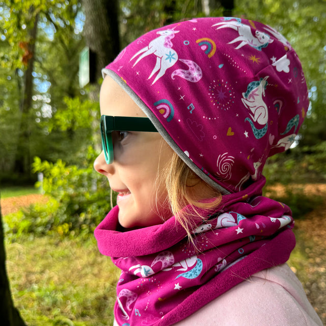 Mädchen trägt Wollhuhn LONG Loop mit Einhörner Beere, ideal für Komfort und Schutz. Handgemacht, vielseitig für Kinder und Erwachsene, wendbar und leicht anzuziehen.
