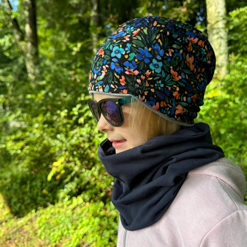 Mädchen trägt Wollhuhn Öko Long Beanie/Wendemütze: zweilagig, aus weichem Baumwolljersey, bequem, ideal für Kinder, handgemacht in Deutschland, mit floralem Muster.