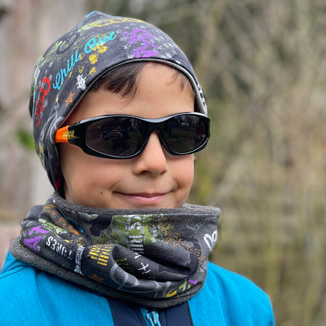 Junge mit Sonnenbrille und Schal trägt Wollhuhn Öko Shorties, eine zweilagige, handgemachte Wendemütze in Anthrazit, ideal für aktive Kinder.