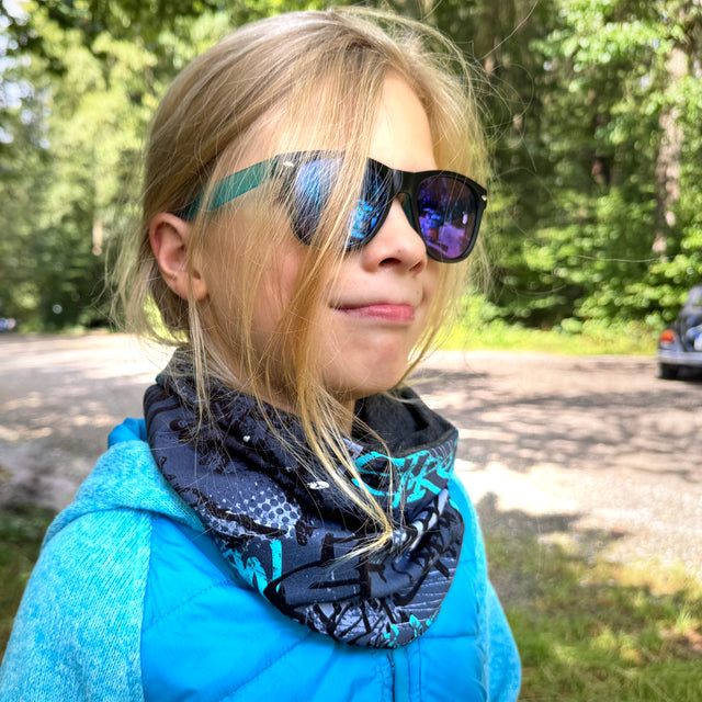 Mädchen mit Sonnenbrille trägt den Wollhuhn LONG Loop, Jersey- oder Fleecefutter, Skater Blau, ein handgemachter, komfortabler Schlauchschal für vielseitigen Schutz.