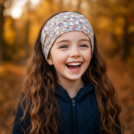 Mädchen trägt Wollhuhn Elastisches Öko Stirnband, lacht draußen im Herbstlicht. Zweilagig, weich, geeignet für Aktivitäten, handgemacht in Deutschland.