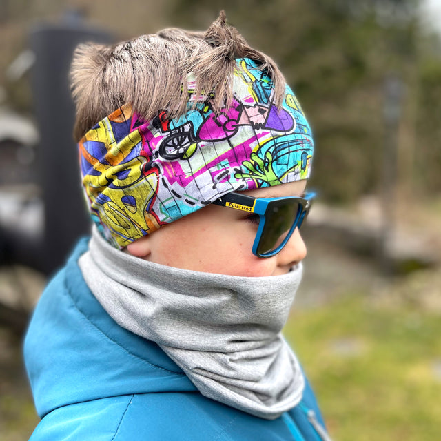 Person trägt Wollhuhn Elastisches Öko Stirnband, Jersey, zweilagig, breit, Graffiti bunt. Ideal für Outdoor-Aktivitäten, handgemacht in Deutschland.