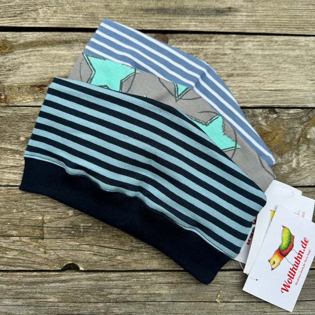 Stapel von Wollhuhn Beanie Überraschungstüten auf Holzoberfläche, handgefertigte Mützen aus hochwertigen Materialien, ideal für Adventskalender oder Geburtstage.
