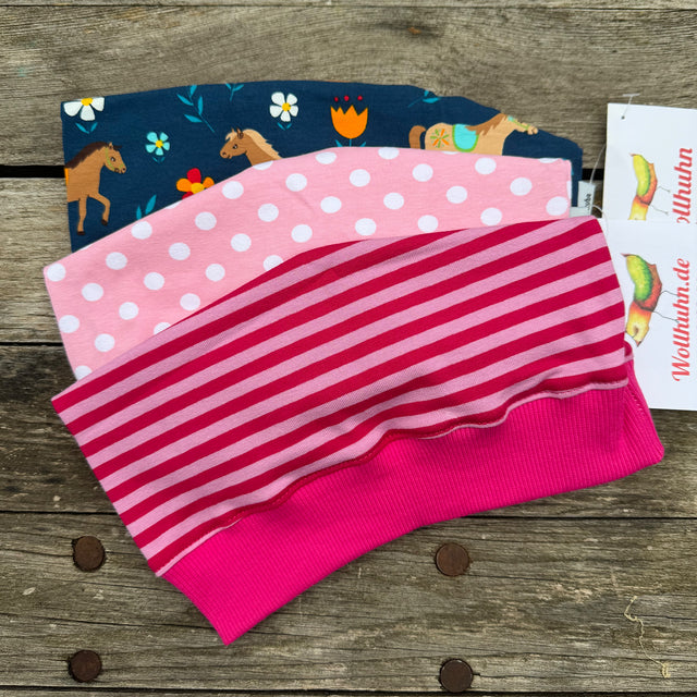 Beanie Überraschungstüte: Stapel von pink-blauen und gestreiften Mützen, handgefertigt in Deutschland, ideal für Adventskalender oder Geschenke. Hochwertige Qualität, nachhaltig produziert.